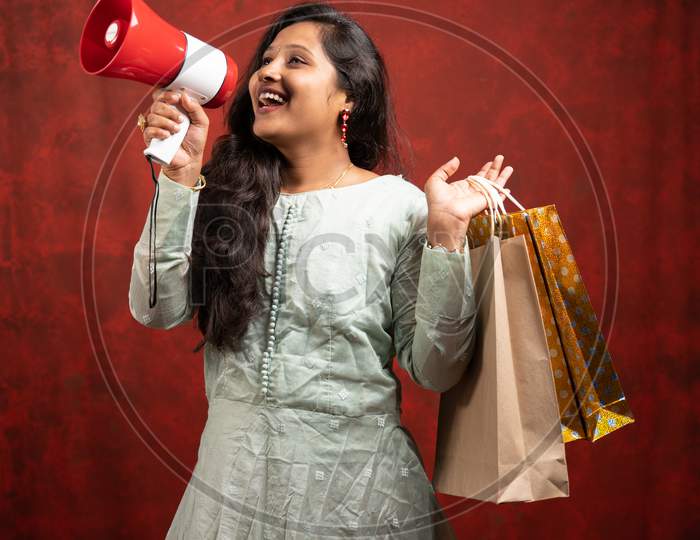 Happy Young Indian Woman Making Annnouncement On Megaphone About Online Or E-Commerce Sales By Holding Shopping Bags - Concept Of Promotion, Special Offers During Festivals.