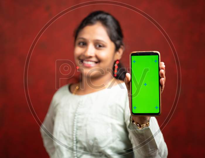 Selective Focous On Smartphone, Happy Smiling Indian Girl In Traditional Dress Showing Mobile Phone With Mock Up Green Screen For Diwali Festival Sale Advertisement By Looking At Camera.