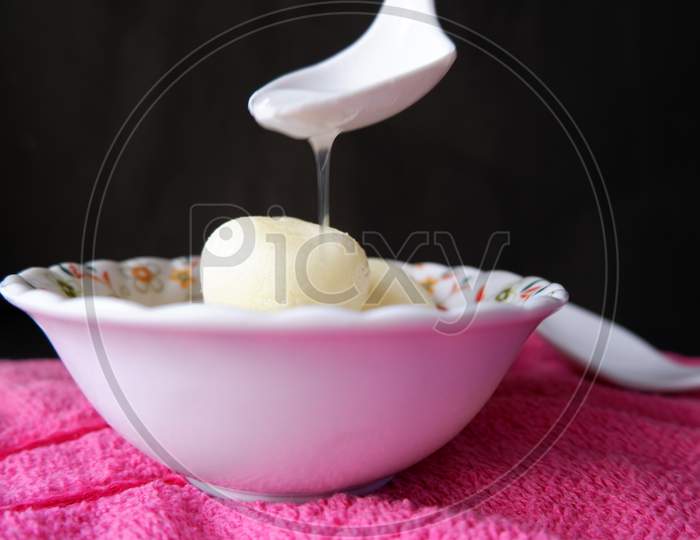 Rasgulla served in white printed bowl and pouring sugar syrup on it by white spoon