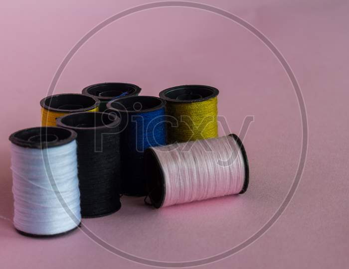 Black Plastic Spools Containing Multi-Colored Thread On A Neutral Pink Background.
