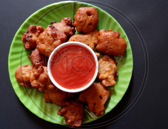 indian pakora and tomato sauce served in green round plate with black background