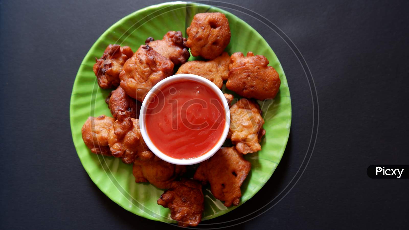 indian pakora and tomato sauce served in green round plate with black background