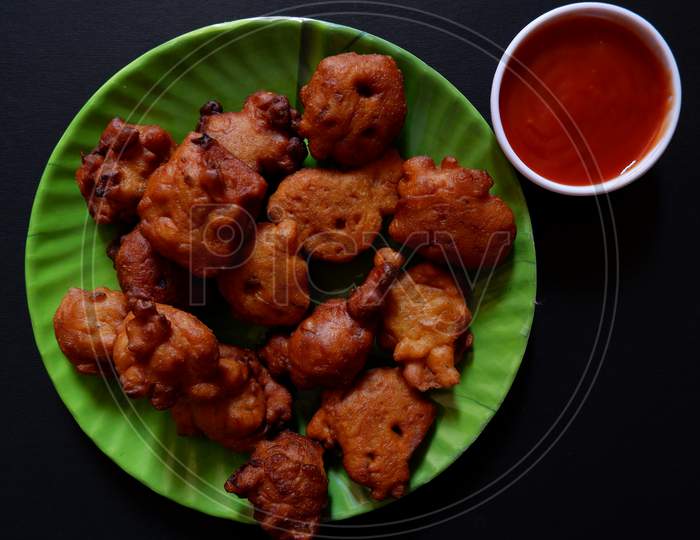 Pakora served in green dish and tomato sauce in small white cup on black background