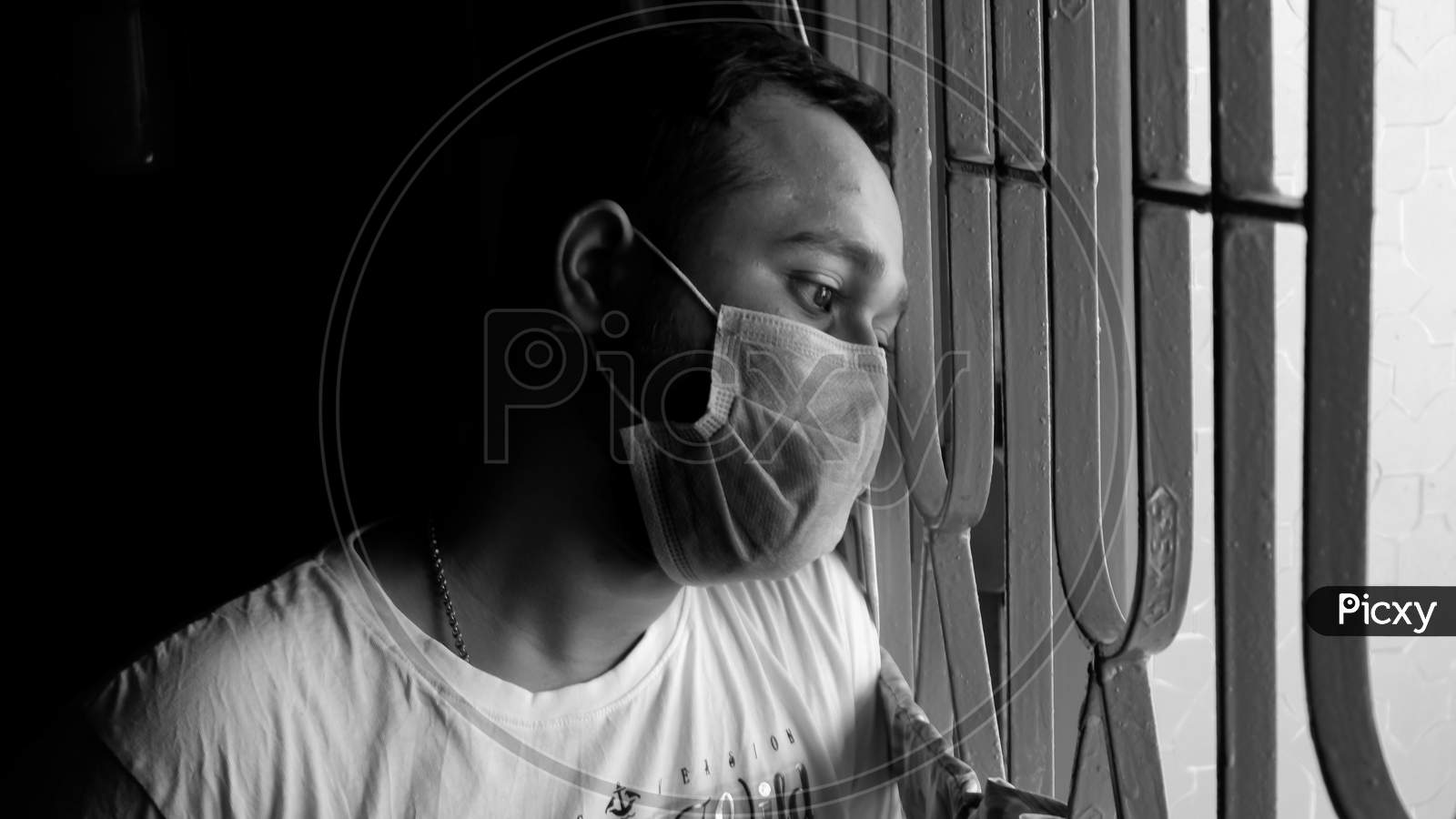 Black And White Image Of Boy With Mask On Face Watching Out Of The Window To Outside Of World With Stressful Expression.
