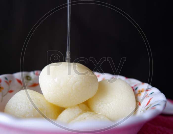 Rasgulla served in white printed bowl and pouring sugar syrup in it