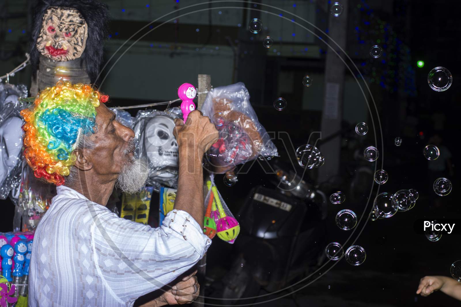 An Old Hawker Wearing Colorful Selling Toys And Creating Bubbles.