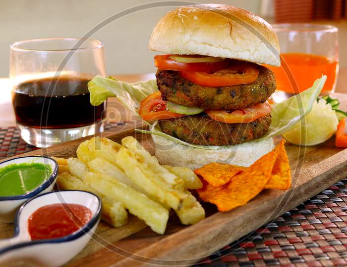 Double decker fully loaded vegetarian burger with dip and french fries in a small cafe.