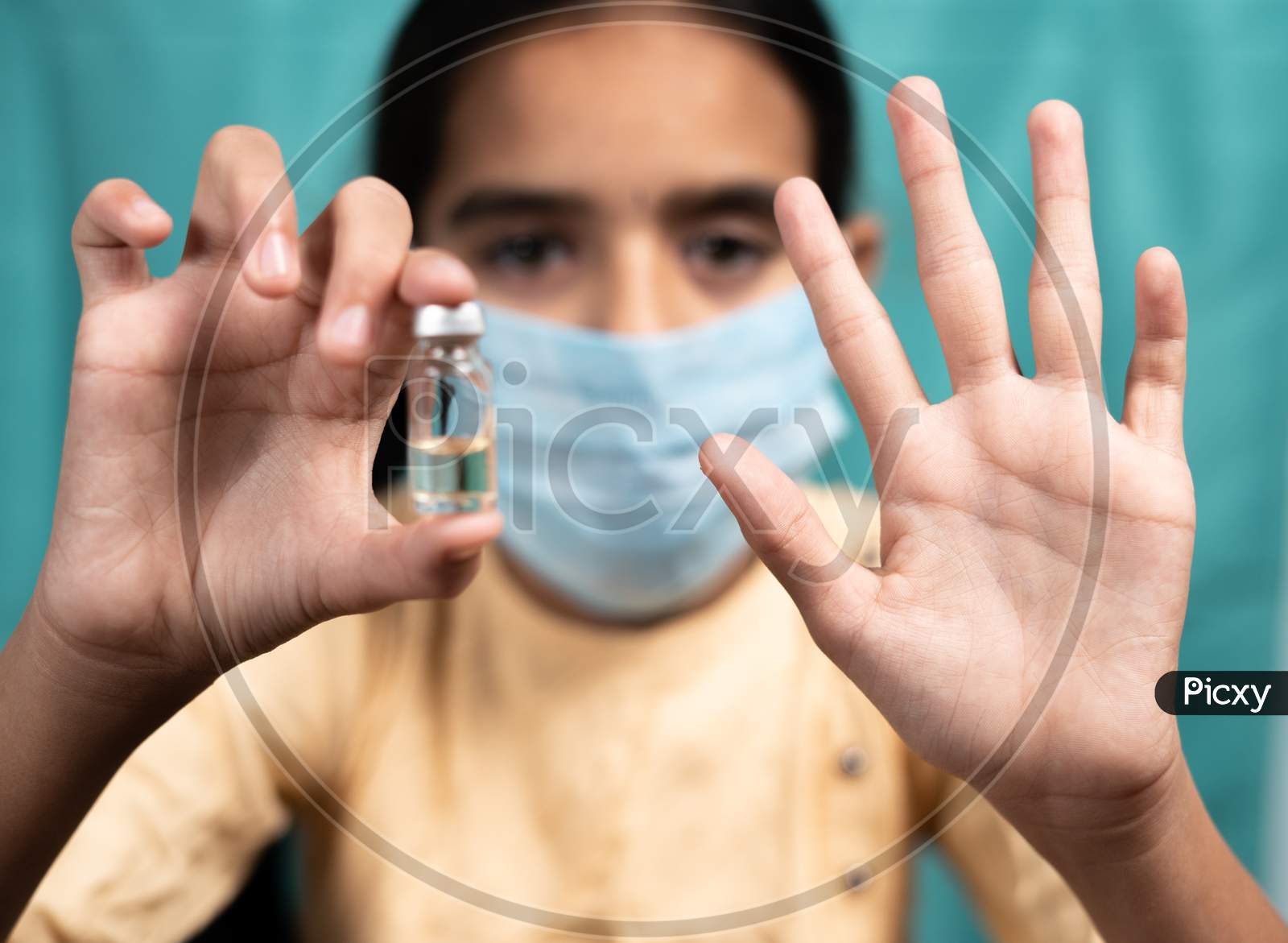 Selective Focus On Hand, Kid Medical Face Mask Saying No To Covid-19 Or Coronavirus Vaccination By Shoing Showing Hand Gesture And Vaccine Bottle - Concept Of Children Vaccine Hesitancy.