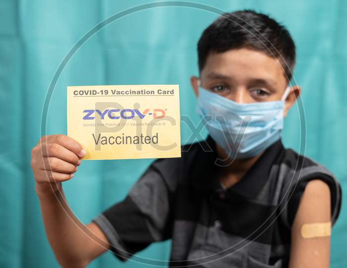 Maski, India - October 26, 2021 : Young Kid With Medical Face Mask Showing Zycov-D Covid-19 Or Coronavirus Vaccinated Report Card.