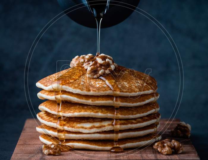 Pouring honey on pancakes with walnuts