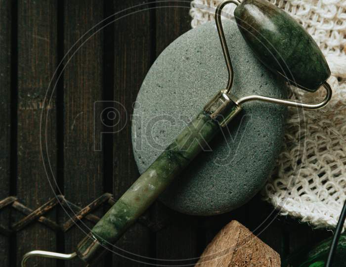Flatlay Of Jade Face Roller Laying On A Grey Stone
