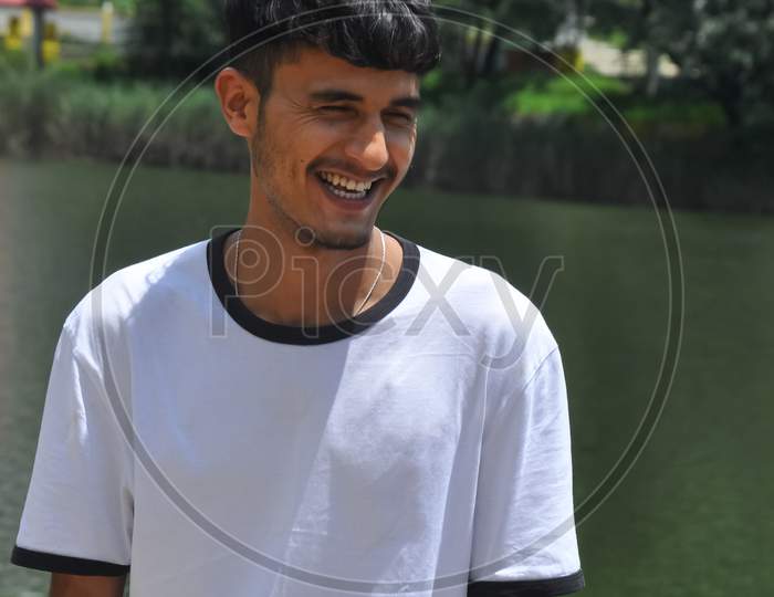 Portrait shot of a Indian young guy standing and smiling beside of lake with wearing white t-shirt
