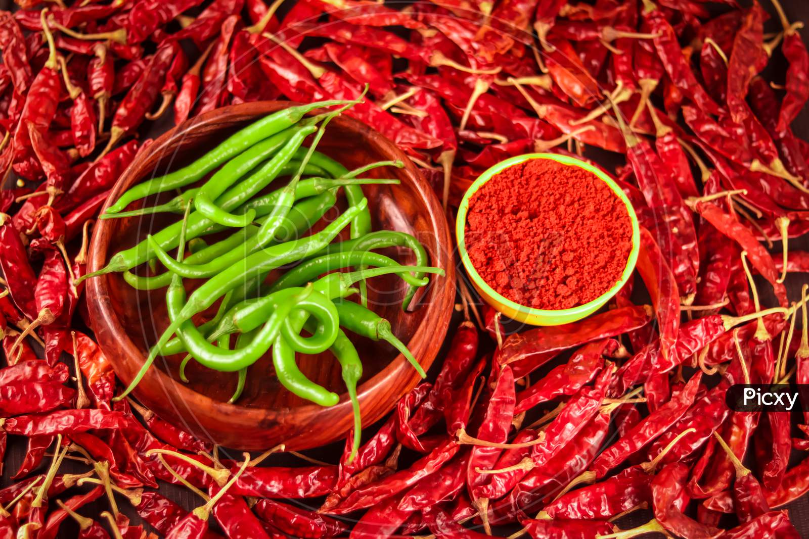 Red Chili Peppers Powder In Yellow Bowl In Wooden Spoon On Chili Peppers Background,Green Chili And Red Chilli,Spices And Bowl With Chilli Pepper On Wooden Background
