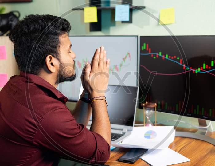 Worried Trader Praying God To Make Profit Or Stock Market To Go Up Infront Of Charts On Computer Screan - Concept Of Risk In Crypto Trading And Investing On Equity Shares.