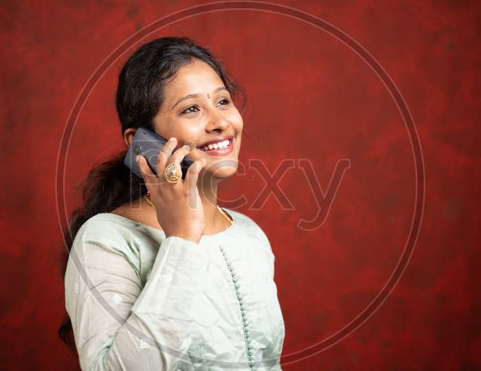 Smiling Indian Girl Busy Talking On Mobile Phone By Looking Above Showing With Copy Space - Concept Of Happy Customer Service And Communication