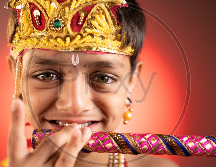 Close Up Head Shot Of Kid In Lord Krishna Costume Playing Flute During Shri Krishna Janmashtami.