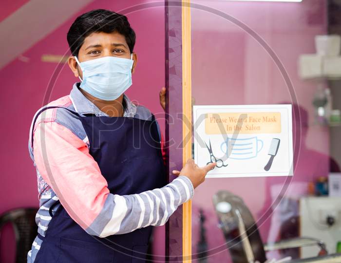 Barber With Medical Mask Showing Wear Mask At Saloon Sign Board To Avoid Coronavirus Or Covid-19 Infection As Safety Measures