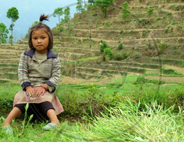 A Nepali girl sitting in open field in hills. Rural life photo.