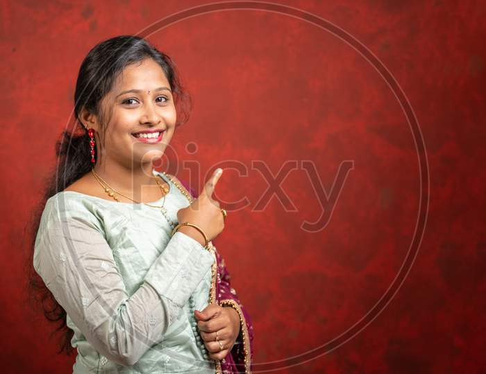 Happy Smiling Indian Girl Pointing Finger Above By Looking Camera - Cocnept Of Showing Offers Or Discounts For Festival Sales Advertisement With Copy Space.
