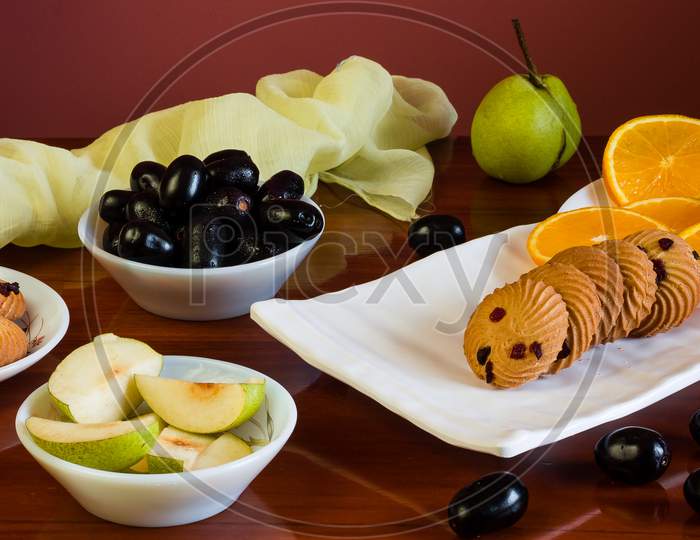 Close-up view of colorful fruit platter with a mix of sweet,fresh fruits like oranges,pears,jamun and oat cookies,isolated on dark wood vintage table as background.