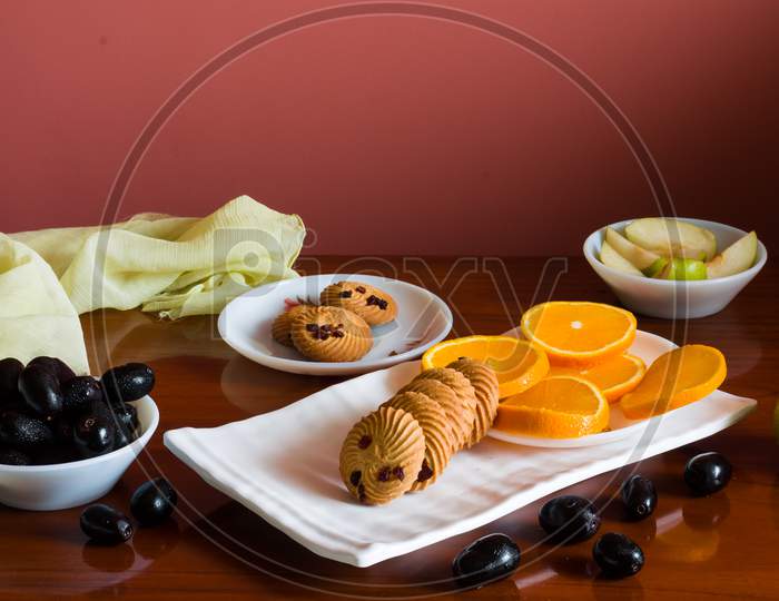Front view of colorful,healthy fruit platter with orange slices,pears,jamun and oat cookies,on a dark  background.Berries scattered around.
