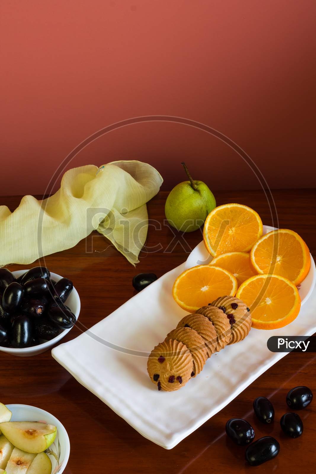 Close-up,top view of fruit platter with a mix of fresh,juicy,sweet orange slices,pears,jamun or java plum berries and healthy oat cookies,on dark wooden table.