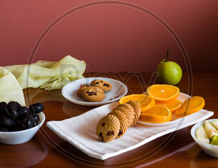 Front view of fruit platter with mix of fresh,juicy,sweet orange slices,pears,jamun or java plum berries and healthy oat cookies,on dark wooden background.