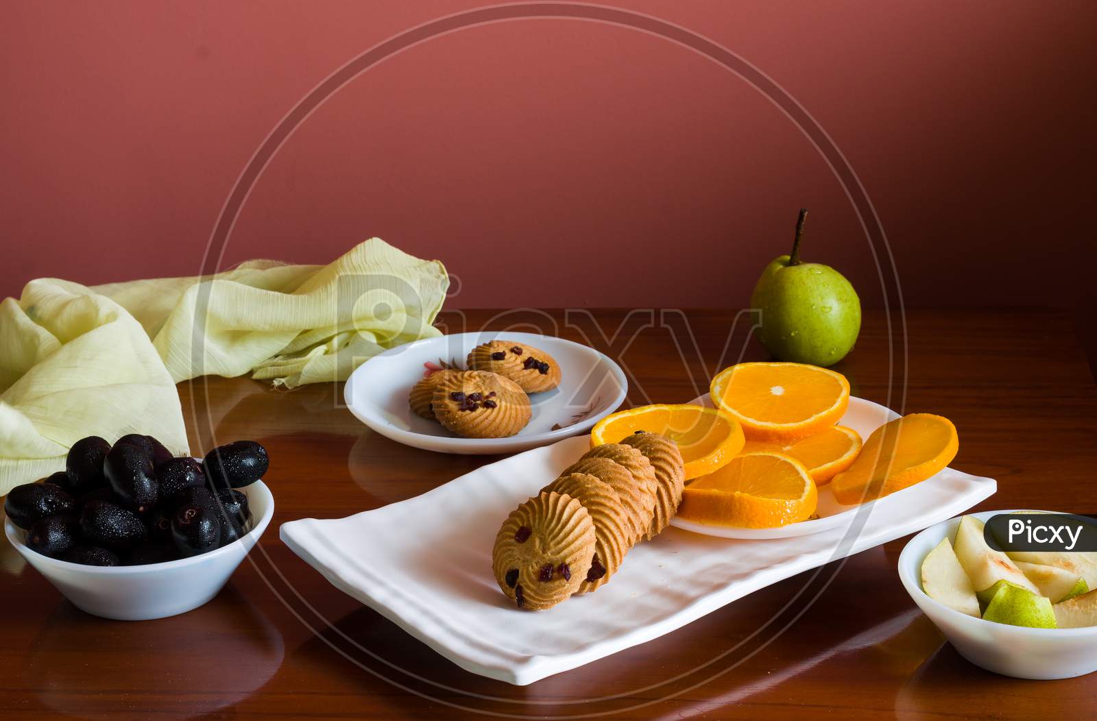 Front view of fruit platter with mix of fresh,juicy,sweet orange slices,pears,jamun or java plum berries and healthy oat cookies,on dark wooden background.
