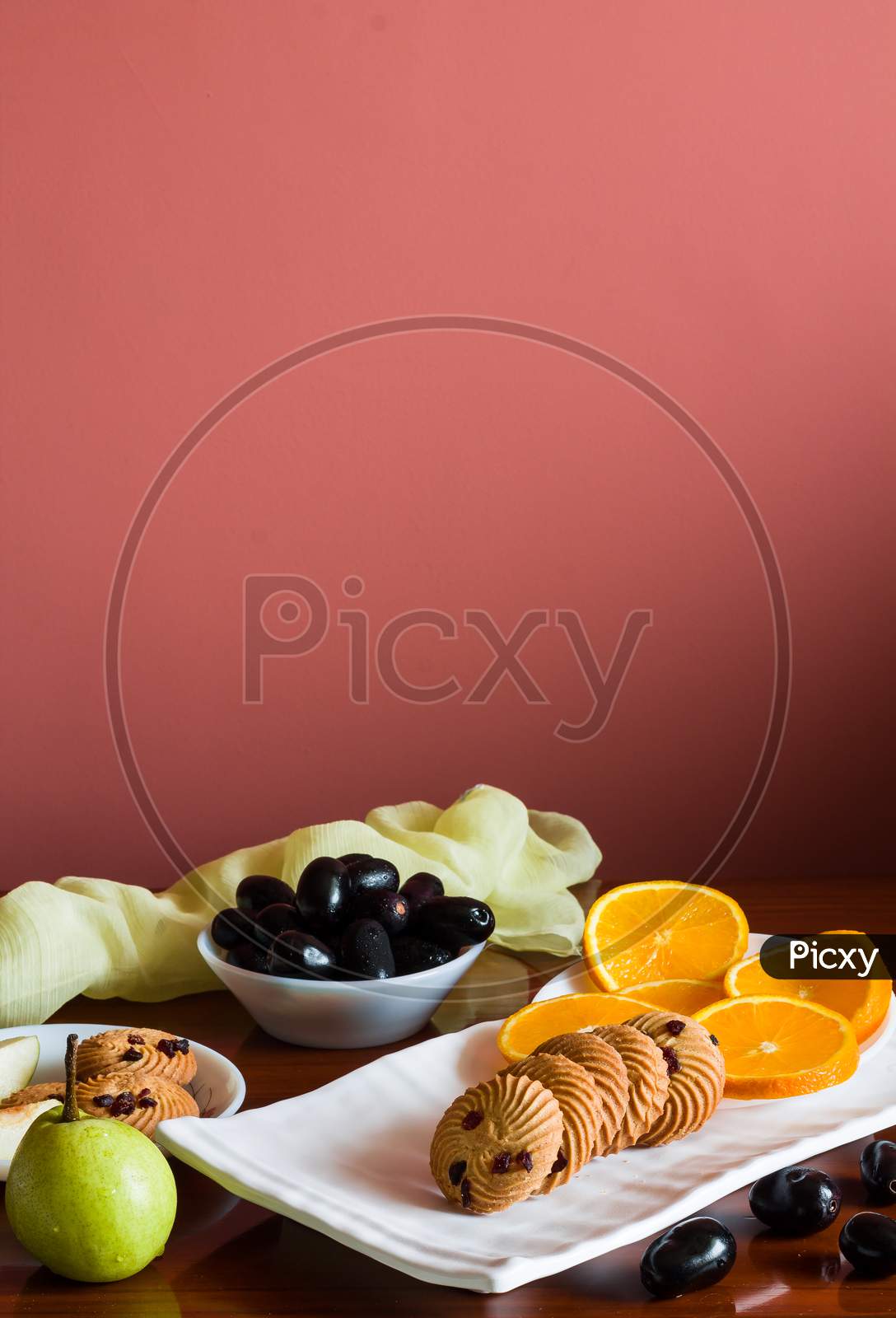 Front view of assortment of fruits in a fruit platter with orange slices,jamun,pears and oats cookies. Healthy mix.Vertical.