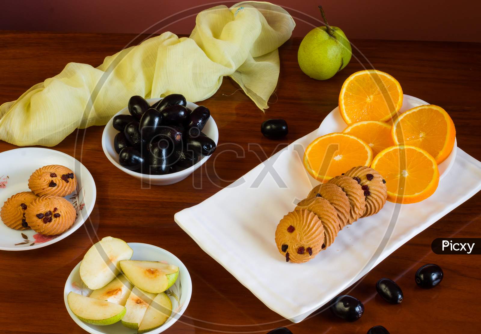 High angle and close-up view of colorful fruits platter with oranges,jamun,pears and cookies,on dark background.