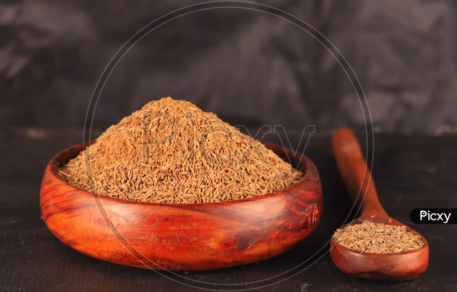 Cumin Seeds On Wooden Spoon And Wooden Bowl,Caraway Spice Seeds On The Wooden Spoon On The Black Scratched Background,