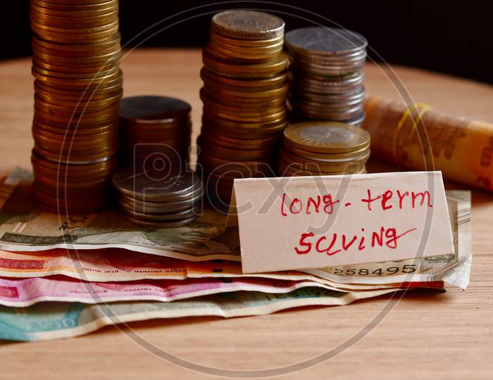 Long Term Written On A Peppers On Black Background,Paper Tag Written With Long Term Saving Inscription,Coins Stack,Jar And Black Background,Saving Money,