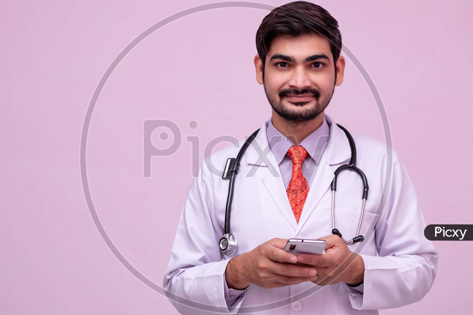 Young Male Doctor Look At Camera And Smiling Holding Smartphone.