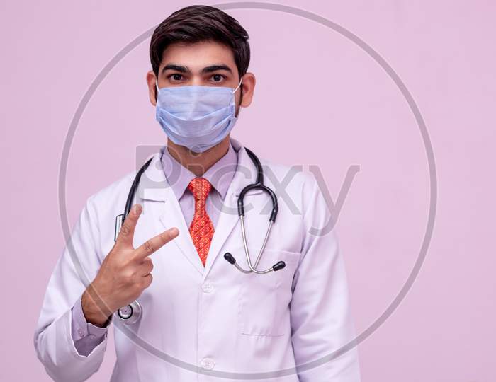 Doctor Wearing Medical Mask Showing Victory With Hand On Isolated Background.
