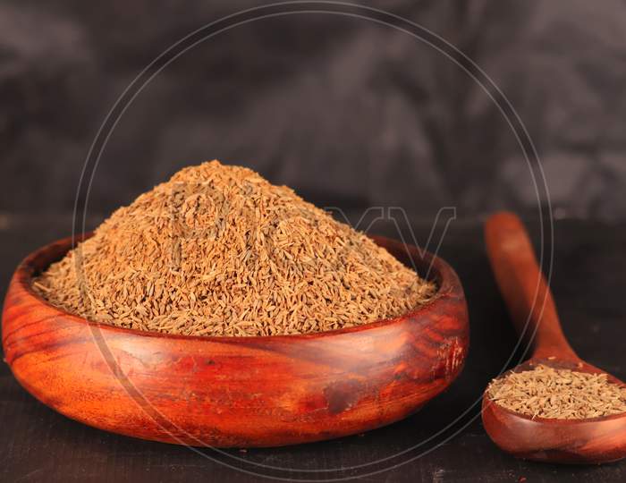 Cumin Seeds On Wooden Spoon And Wooden Bowl,Caraway Spice Seeds On The Wooden Spoon On The Black Scratched Background,