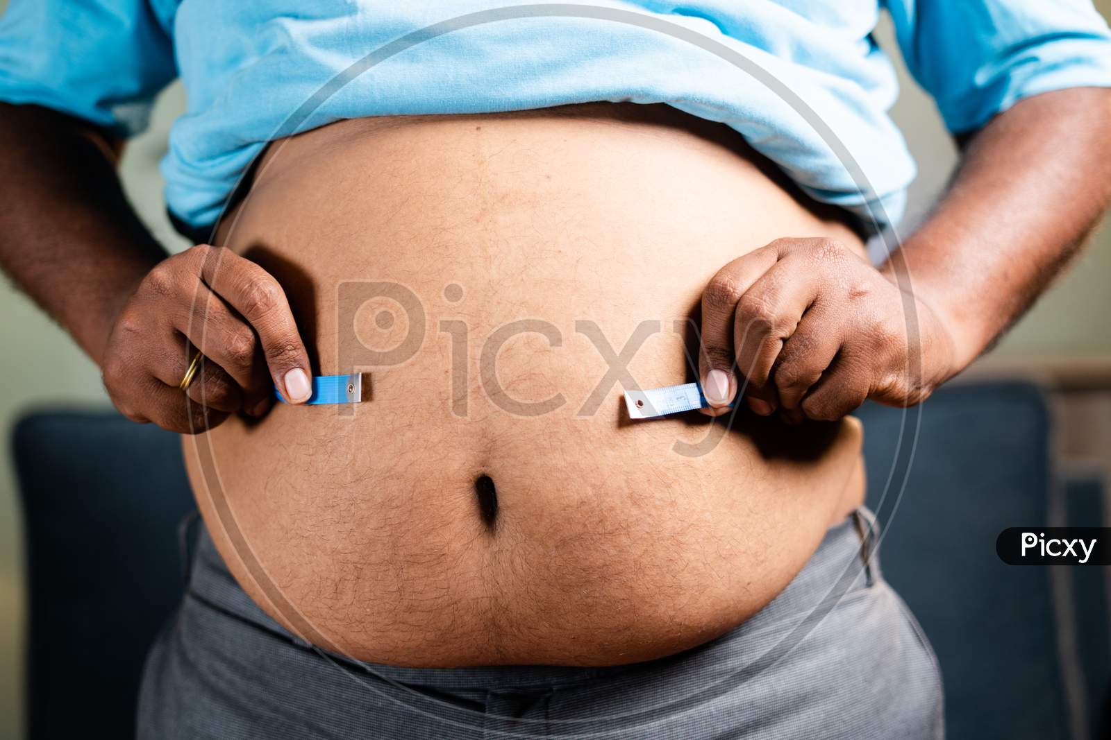 Unrecognizable Unhealthy Obese Man Checking Stomach Or Waist Fat Using Measuring Tape Before Diet At Home - Concept Of Suffering Body Overweight Due To Junk Food Habits.