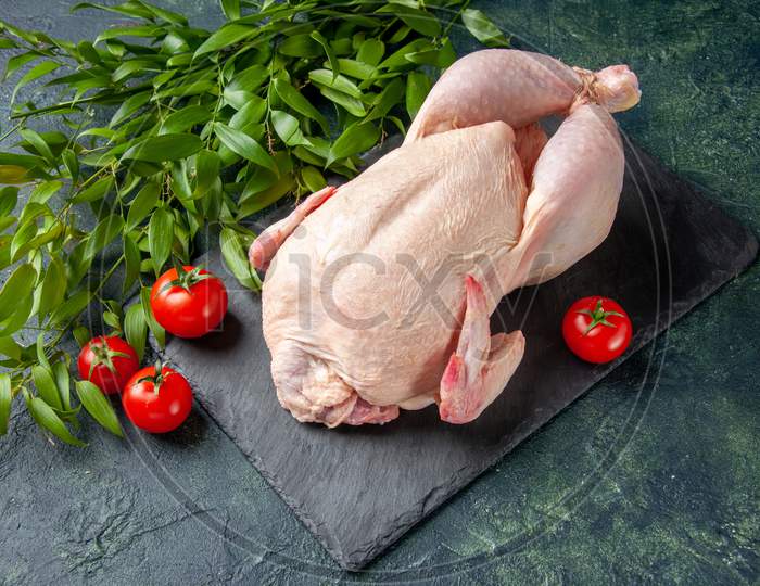 Half-Top View Fresh Raw Chicken With Green Leaves On Dark surface.