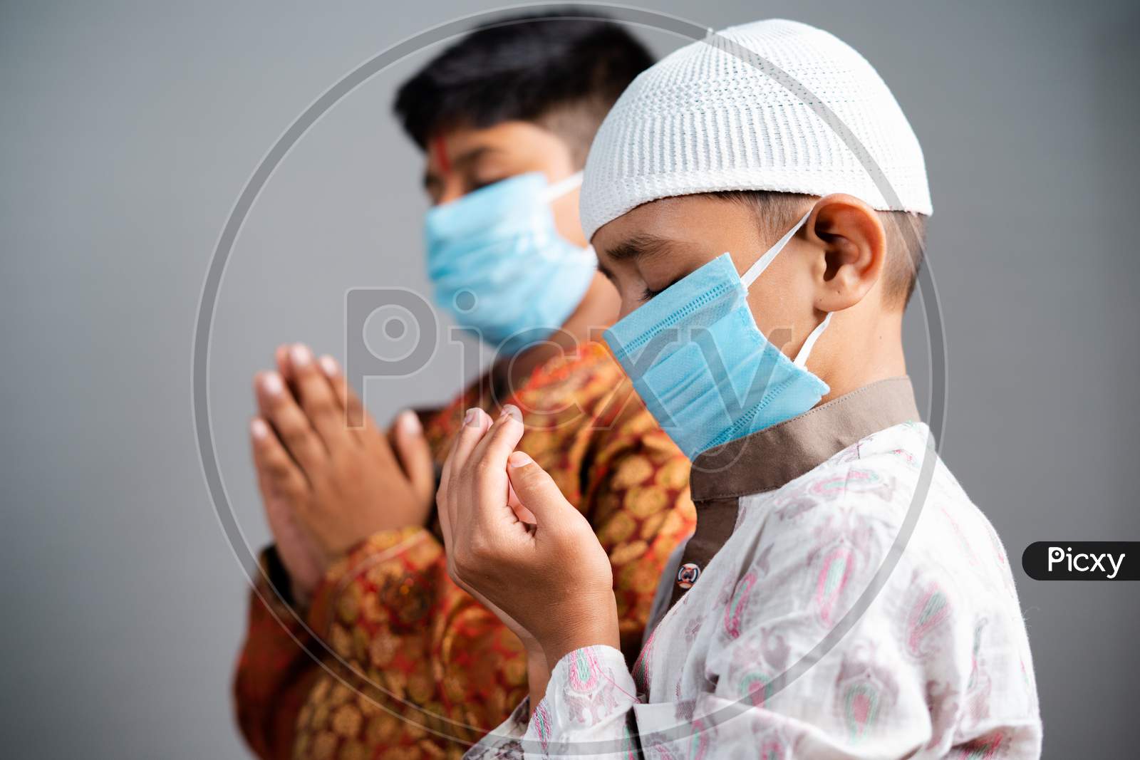 Multiethnic Kids With Medical Face Mask Praying Together By Folding Hands To Protect From Coronavirus Pandemic - Concept Of Friendship, Communal Harmony During Covid-19 Outbreak
