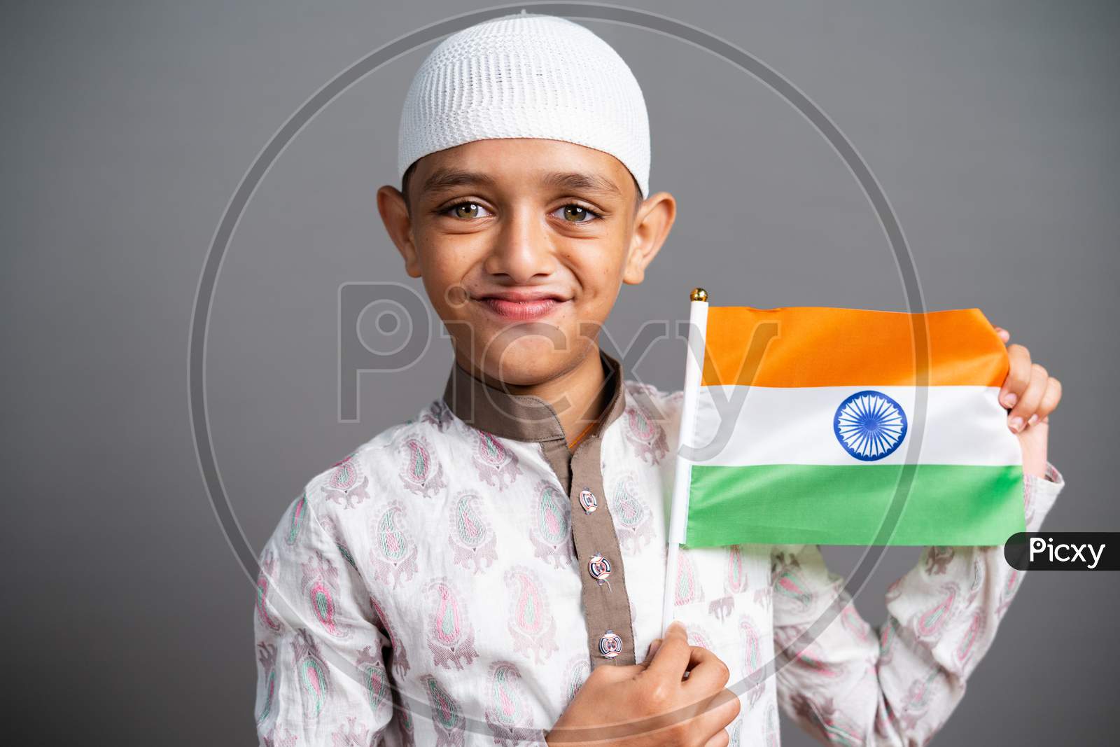 Portrait Shot Of Happy Muslim Kid With Indian Flag In Hand Saluting By Looking Camera - Concept Of Nationalism, Patriotism, Republic Or Independence Celebration.