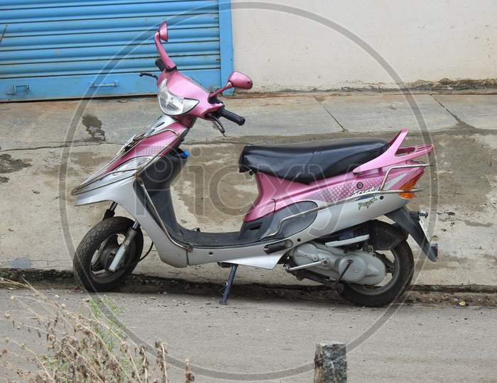 Closeup Of Tvs Scooty Pep Plus Princess Pink Colour Scooter Parking In Front Of Gate On Roadside
