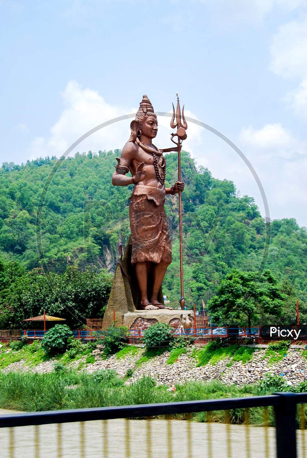 Lord Shiva Tall Statue With Snake Near Har Ki Pauri Haridwar, Hindu God Idol Mahadev At A Garden With Blue Sky Background And Mountains