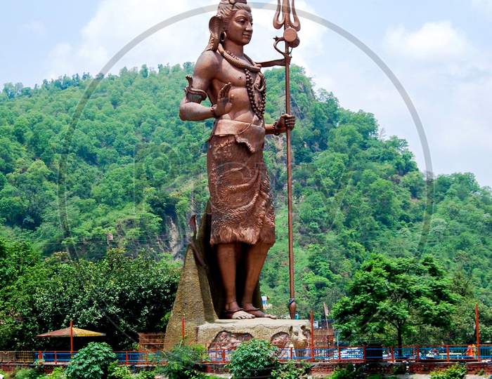 Lord Shiva Tall Statue With Snake Near Har Ki Pauri Haridwar, Hindu God Idol Mahadev At A Garden With Blue Sky Background And Mountains