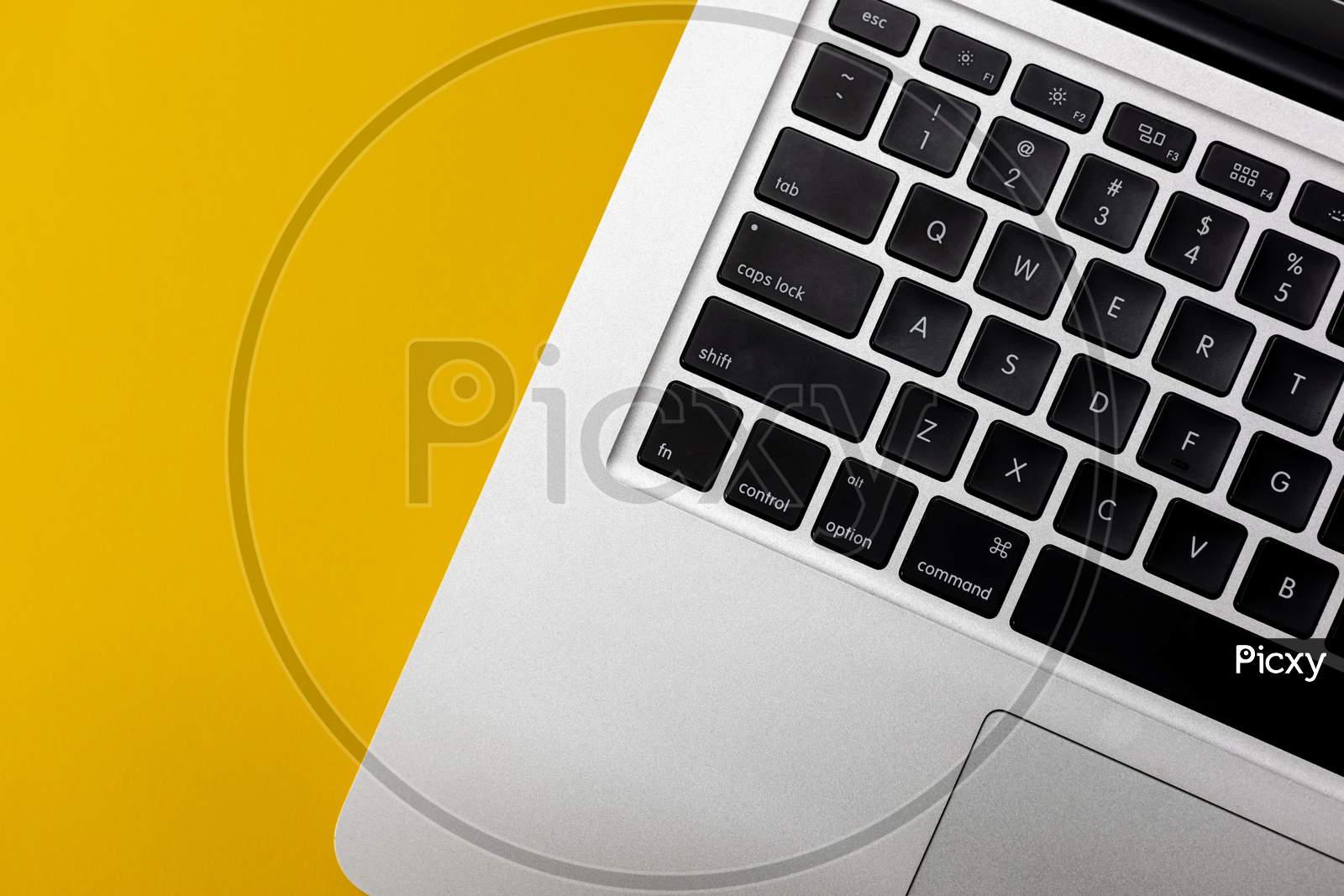 Flat lay, top view of Laptop computer keyboard on a bright yellow background. Closeup macro aesthetic profile shot of keyboard. Work from home WFH workspace - angle 2