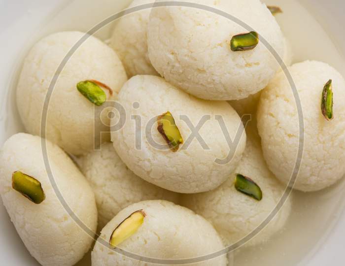 Rasgulla Or Rosogulla - An Indian Sweet Made From Khoya, Soft And Spongy, In Earthen Bowl Over Yellow Napkin And Brown Background