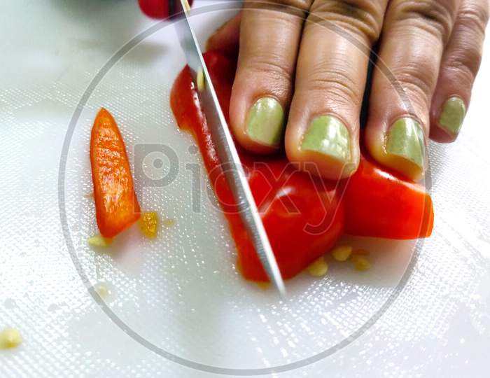Slicing Sweet Red Pepper On Cutting Board. Female Hand Cuts Caps