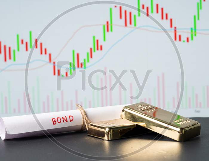 Concept Of Gold Bond Showing With Gold Bars And Bod Paper With Stock Market Graphs Or Charts In Background.