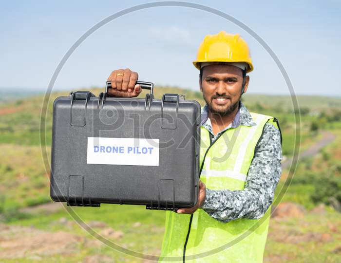 Focus On Case Drone, Pilot With Protective Work Wear And Hard Hat Showing Drone Case By Looking Camera - Concept Of Professional Uav Operator Or Aerial Filmmaker