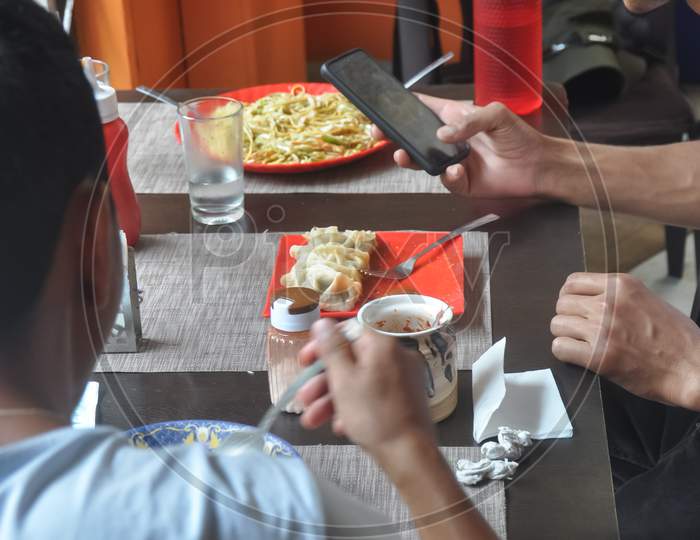 Two guys eating chinese food and taking picture of food with mobile phone
