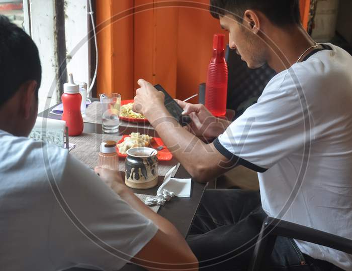 Two guys eating chinese food and taking picture of food with mobile phone