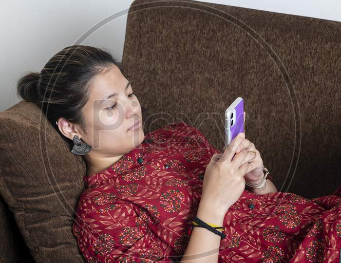 Young Indian Girl Using Her Mobile Phone While Lying Down On The Couch.Lifestyle And Technology Concept.